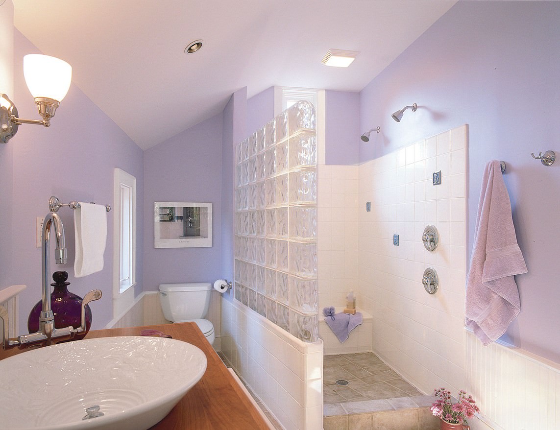 دکوراسیون حمام و دستشویی با رنگ اصلی و دیوار و سقف بنفش پاستلی که اتاق دوش با کاشی سفید و توالت فرنگی سفید و روشویی چوبی دارد